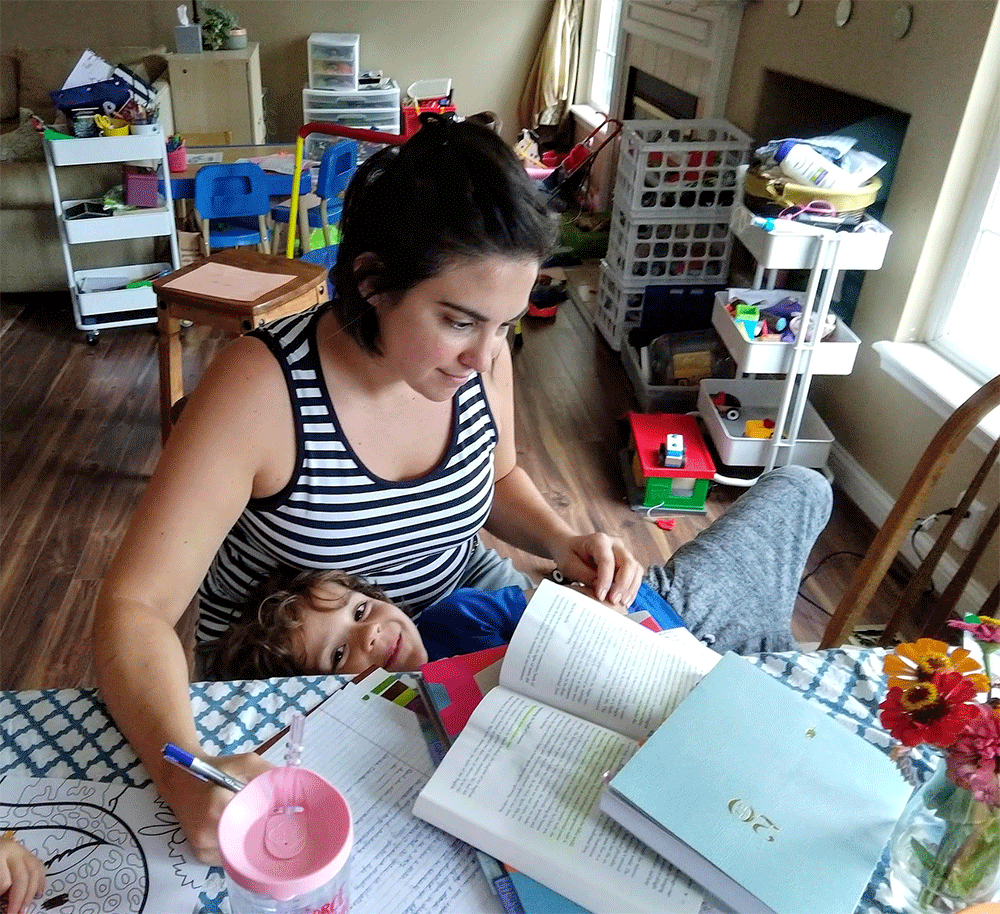 Jen is pictured studying with her Bible and notebook in a white and black striped tank top while her son in a blue shirt is seated in her lap.