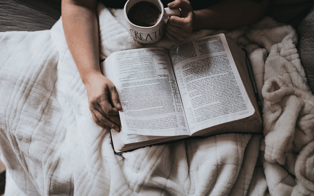 Picture of someone studying Stephen's story in the book of Acts while sitting under a cream cozy blank drinking coffee from a white mug that says "CREATE" in black letters in a modern typeface.