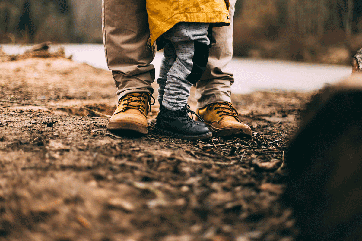 The feet of a Dad in khakis and a little boy in a yellow jacket are pictured standing outside to represent the love a father has for his children.