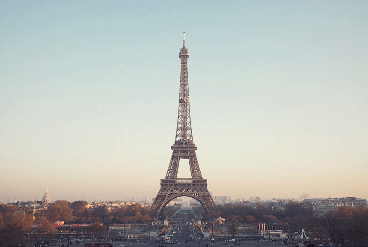 The Eiffel Tower is seen from a distance with a sunrise in the background.
