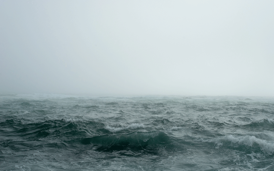 A choppy turquoise sea is pictured with a foggy gray sky in the background.
