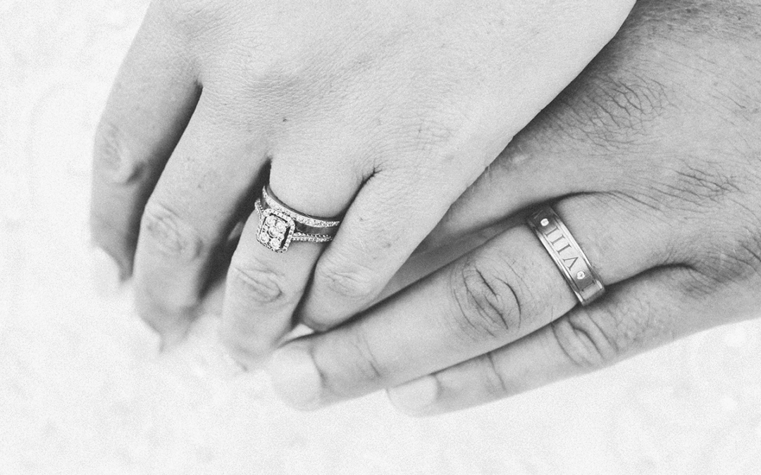 Black and white photo of man and a woman holding hands showing wedding bands.